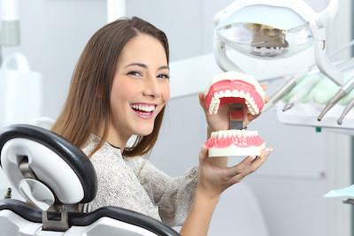 A woman holding a tooth model in a dental office