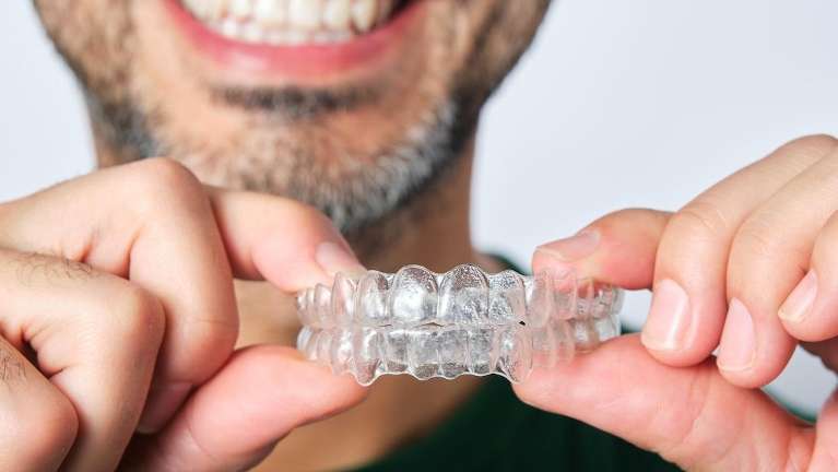 A smiling man holding his Invisalign clear aligners